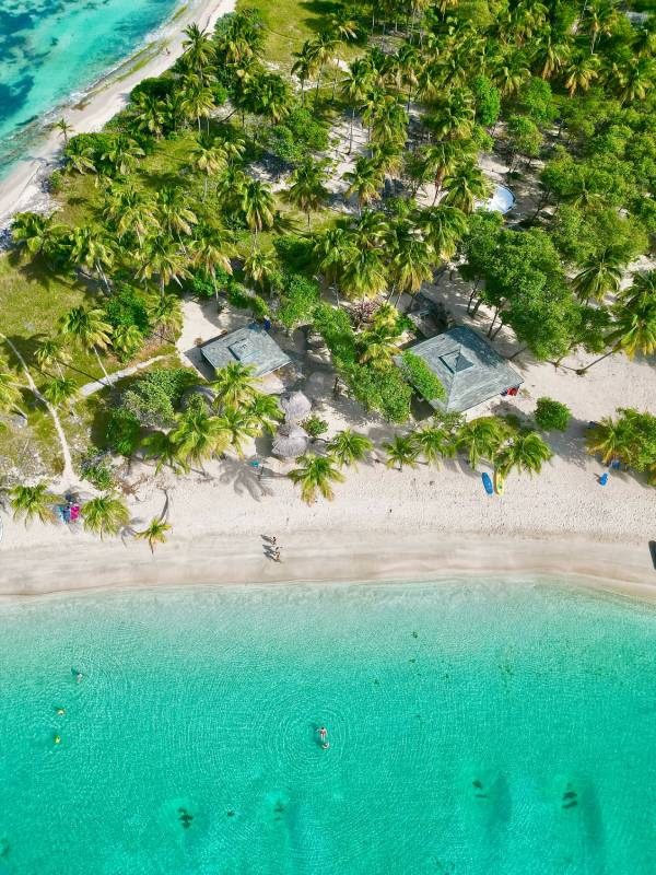 Aerial view of a white-sand Grenadines beach with turquoise water, palm trees and shaded cabanas.